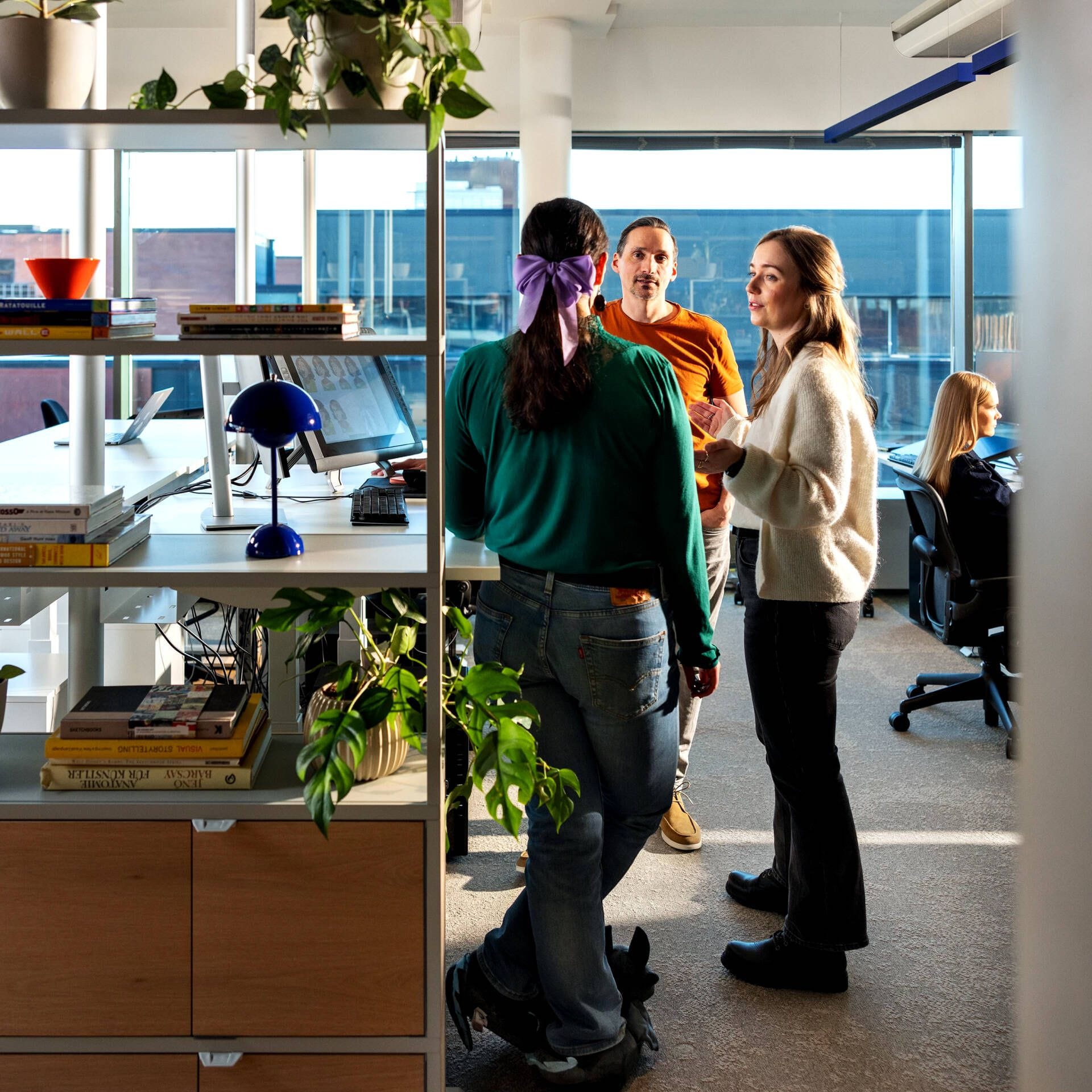 Metacoreans standing by their desks and shelves filled with plants and books.